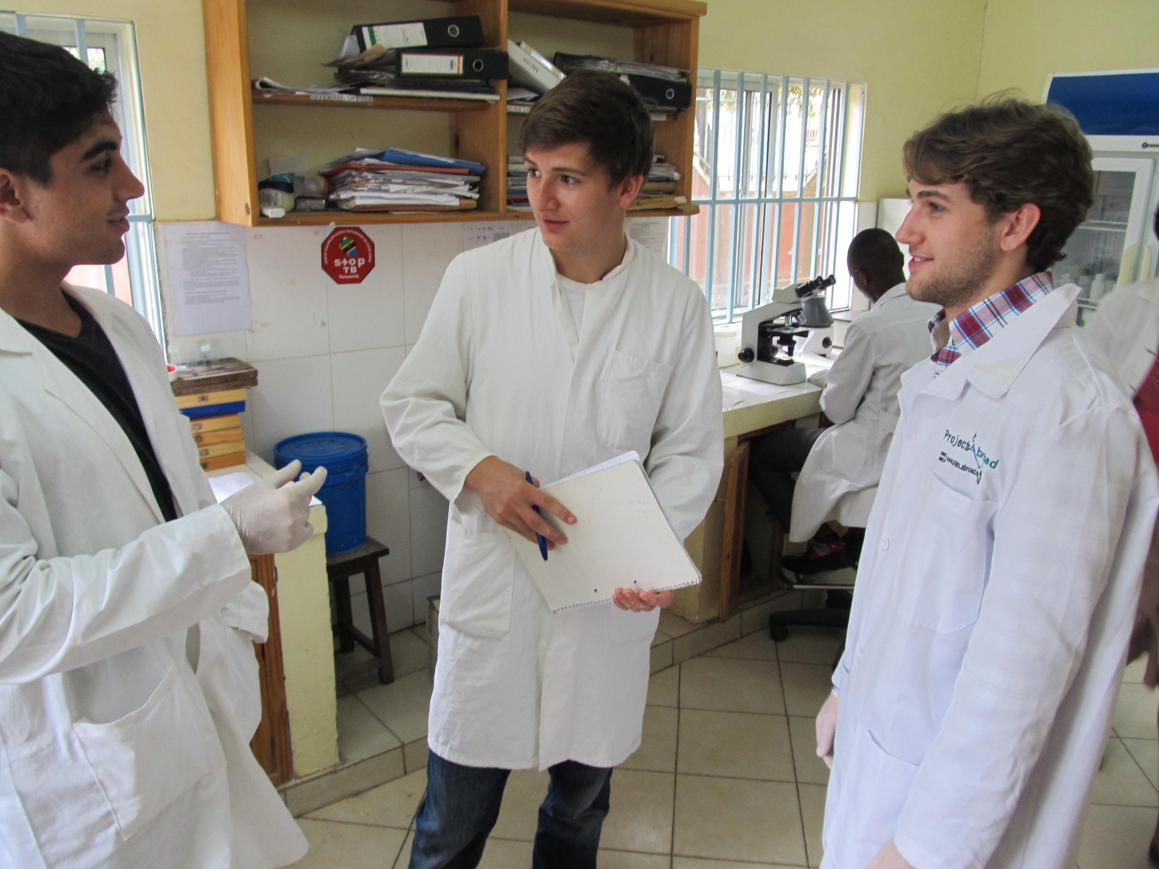 Projects Abroad interns discuss a patients file in a dental clinic during their Dental internship in Tanzania. Male Dentistry interns are in white lab coats discussing a patient's file during their dentistry work experience in Tanzania.